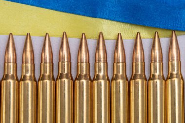 Ukrayna bayrağı şeritleri ve Kalaşnikof saldırı tüfeği için 7.62 kalibrelik fişekler, seçici odaklanma. Konsept: Ukrayna 'da kiralık silahların tedarik edilmesinde yardım,