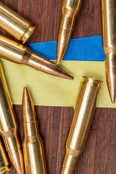 Ukrayna bayrağı şeritleri ve Kalaşnikof saldırı tüfeği için 7.62 kalibrelik fişekler, seçici odaklanma. Konsept: Ukrayna 'da kiralık silahların tedarik edilmesinde yardım,