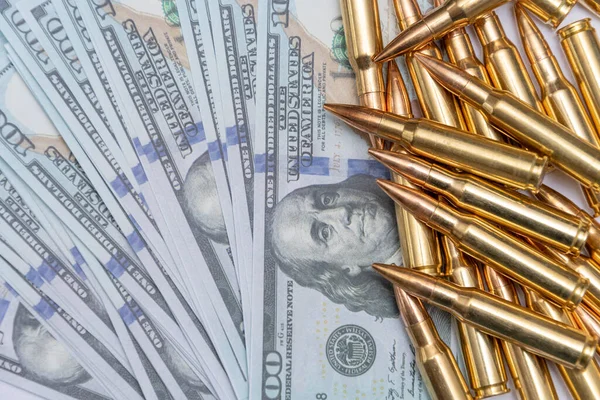 Scattered cartridges with bullets on 100 dollar bills, close-up, selective focusing. Concept: sale of weapons under lend-lease, assistance with weapons, mercenary in the army, trade in ammunition.