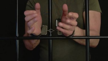 Hüküm giymiş bir adam karanlık bir arka planda parmaklıkların arkasındaki bir hücrede kelepçelenir. Konsept: Mahkemenin mahkuma verdiği hüküm, hapis ve ceza..