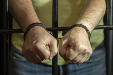 Hapisteki hücrede kelepçeli bir adam. Kavram: Mahkeme salonunda bir mahkum, hüküm giymiş birine verilen mahkeme kararı, hapis cezası.