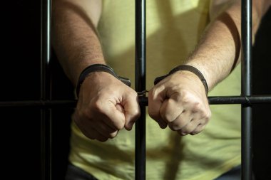 Hapisteki hücrede kelepçeli bir adam. Kavram: Mahkeme salonunda bir mahkum, hüküm giymiş birine verilen mahkeme kararı, hapis cezası.