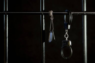 Polis kelepçeleri bir hapishane hücresinin parmaklıklarına bağlanmış karanlık bir arka planda, ordu kimlik kartı, seçici odaklanma. Kavram: bir askerin yargılanması, bir savaş suçu..