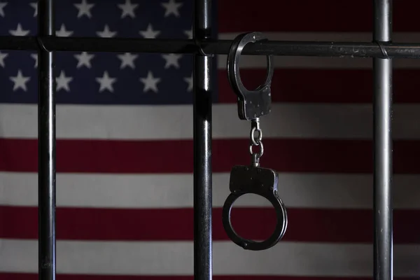 Polis Kelepçeleri Hapishane Hücresinin Parmaklıklarına Amerikan Bayrağının Arka Planına Bağlıdır — Stok fotoğraf
