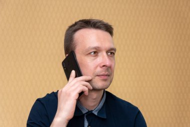 Orta yaşlı bir adam arıyor ve tarafsız bir arkaplanda cep telefonuyla konuşuyor..