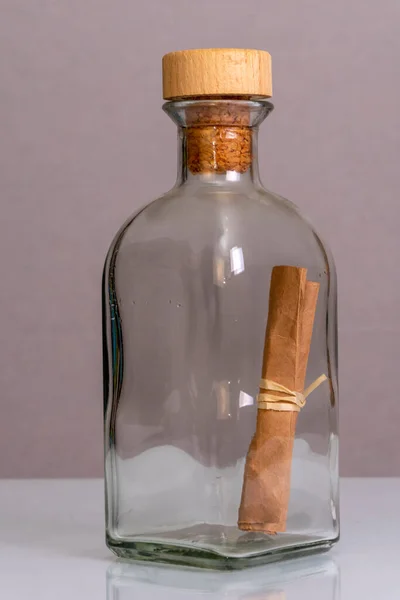 A folded old paper note in a glass bottle with a cork on a blurry background. Concept: sea mail, a message from an island, a request for help, a shipwreck, a manuscript or parchment.