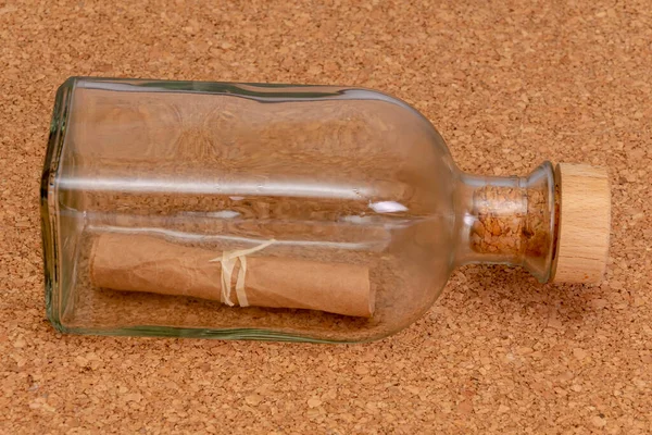 A folded old paper note in a glass bottle with a cork on a textured background. Concept: sea mail, a message from an island, a request for help, a shipwreck, a manuscript or parchment.