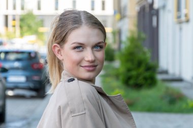 20-25 yaşlarında, açık renk yağmurluk giymiş genç ve güzel sarışın bir kızın sokak portresi..