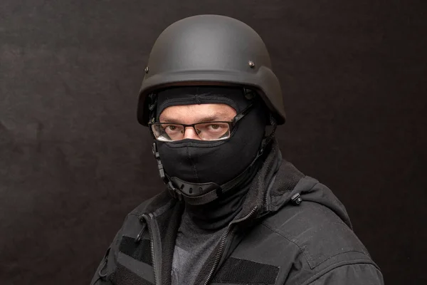 Portrait of a military man with glasses, wearing a bulletproof vest and balaclava, an army helmet on his head, black background. Concept: military journalist, volunteer at war, war in Ukraine, civil self-defense, army unit.