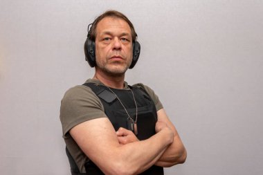 45-50 yaşlarında, kurşun geçirmez yelek ve arka planda çekim yapmak için taktik kulaklık takan yaşlı bir adam..