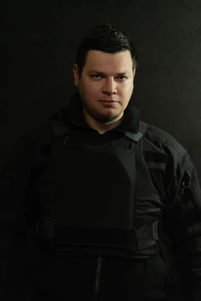Portrait of a military man in a bulletproof vest and black uniform on a dark background. Concept: volunteer for war, war in Ukraine, civil self-defense.