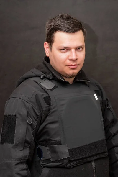 Portrait of a military man in a bulletproof vest and black uniform on a dark background. Concept: volunteer for war, war in Ukraine, civil self-defense.