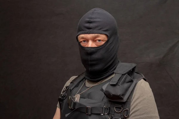 Portrait of a military man 45-50 years old in a bulletproof vest and balaclava on a dark background. Concept: volunteer for war, war in Ukraine, civil self-defense.