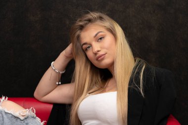 20-25 yaşlarında uzun saçlı bir sarışının portresi. Siyah bir arka planda, kolunda bileziğiyle..