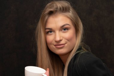 Uzun saçlı, 20-25 yaşlarında, siyah arka planda beyaz fincanı olan bir sarışın..