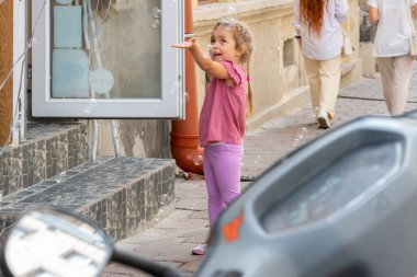 A blonde little 4-year-old girl catches soap bubbles with her hands on the blurry background of the old city in summer
