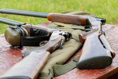 Sporting double-barreled rifles and headphones for shooting lie on a wooden table against the background of the shooting range, bench target shooting.