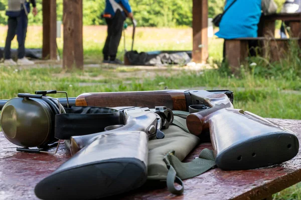 Sporting double-barreled rifles and headphones for shooting lie on a wooden table against the background of the shooting range, bench target shooting.