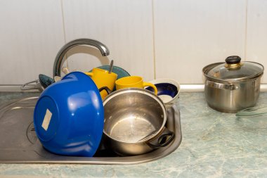 Dirty and unwashed dishes are stacked in the kitchen sink. Unwashed cups, plates, pots, forks and spoons.The height of the water tap determines the number of dishes in the sink.