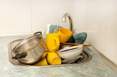 Dirty and unwashed dishes are stacked in the kitchen sink. Unwashed cups, plates, pots, forks and spoons.The height of the water tap determines the number of dishes in the sink.