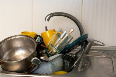 Dirty and unwashed dishes are stacked in the kitchen sink. Unwashed cups, plates, pots, forks and spoons.The height of the water tap determines the number of dishes in the sink.