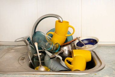 Dirty and unwashed dishes are stacked in the kitchen sink. Unwashed cups, plates, pots, forks and spoons.A mountain of untidy and used dishes.