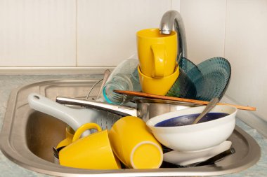 Dirty and unwashed dishes are stacked in the kitchen sink. Unwashed cups, plates, pots, forks and spoons.A mountain of untidy and used dishes.