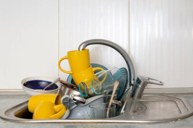 Dirty and unwashed dishes are stacked in the kitchen sink. Unwashed cups, plates, pots, forks and spoons.A mountain of untidy and used dishes.