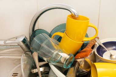 Dirty and unwashed dishes are stacked in the kitchen sink. Unwashed cups, plates, pots, forks and spoons.The height of the water tap determines the number of dishes in the sink.