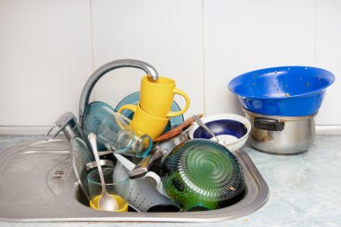 Dirty and unwashed dishes are stacked in the kitchen sink. Unwashed cups, plates, pots, forks and spoons.A mountain of untidy and used dishes.