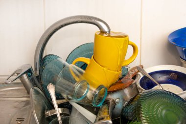 Dirty and unwashed dishes are stacked in the kitchen sink. Unwashed cups, plates, pots, forks and spoons.A mountain of untidy and used dishes.