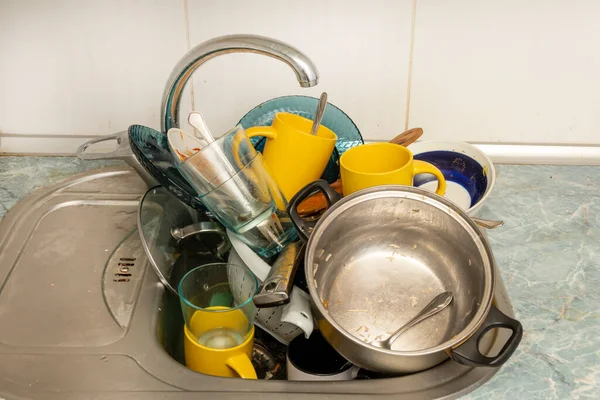 Dirty and unwashed dishes are stacked in the kitchen sink. Unwashed cups, plates, pots, forks and spoons.The height of the water tap determines the number of dishes in the sink.