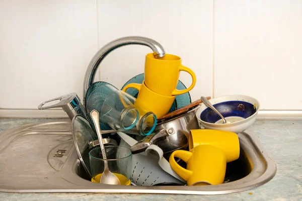 Dirty and unwashed dishes are stacked in the kitchen sink. Unwashed cups, plates, pots, forks and spoons.A mountain of untidy and used dishes.
