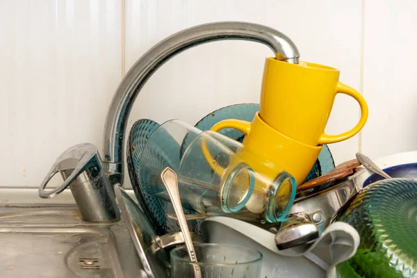 Dirty and unwashed dishes are stacked in the kitchen sink. Unwashed cups, plates, pots, forks and spoons.The height of the water tap determines the number of dishes in the sink.