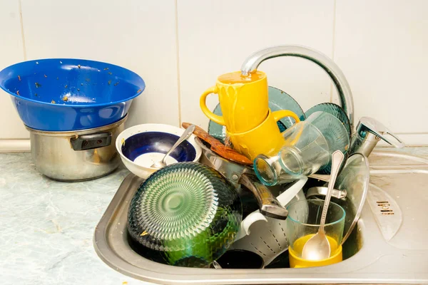 Dirty and unwashed dishes are stacked in the kitchen sink. Unwashed cups, plates, pots, forks and spoons.A mountain of untidy and used dishes.