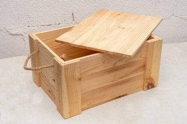 open Wooden box with a lid made of boards with a rope handle, on a textured light background, storage and transportation of objects.