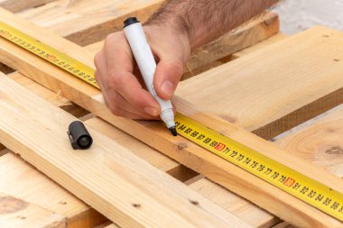 The carpenter puts a marker marker, measures a wooden board with a tape measure, close-up.