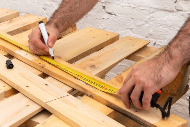 The carpenter puts a marker marker, measures a wooden board with a tape measure, close-up.