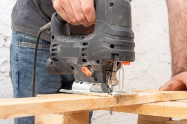 A carpenter cuts a wooden board with an electric jigsaw. Carpentry close-up.