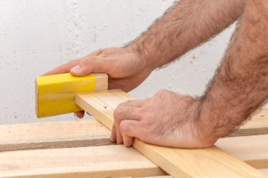 The carpenter cleans and grinds by hand with a bar with sandpaper wooden boards, close-up. Concept: woodworking, manual labor.