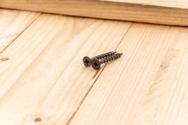 Two black screws are lying on a homemade wooden table, close-up, selective focus.