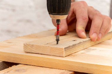 Close-up of an old electric screwdriver in hand, the screw is screwed into a new wooden board. Concept: home improvement, furniture repair.
