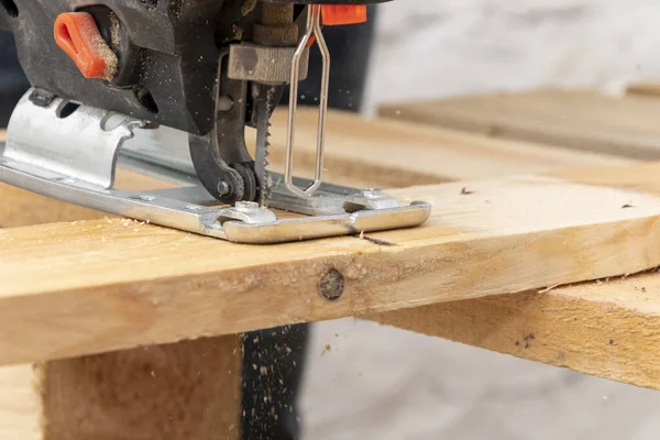 A carpenter cuts a wooden board with an electric jigsaw. Carpentry close-up.