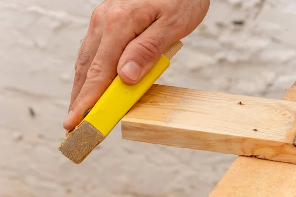 The carpenter cleans and grinds the corners of wooden boards by hand with a bar with sandpaper.