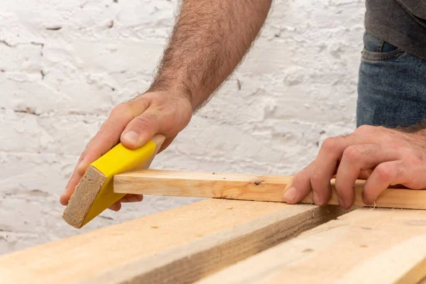 The carpenter cleans and grinds the corners of wooden boards by hand with a bar with sandpaper. Concept: woodworking, manual labor.