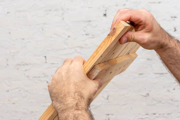 Close-up of a carpenter\'s hands holding a table made of wooden planks. Concept: home improvement, furniture repair with your own hands.