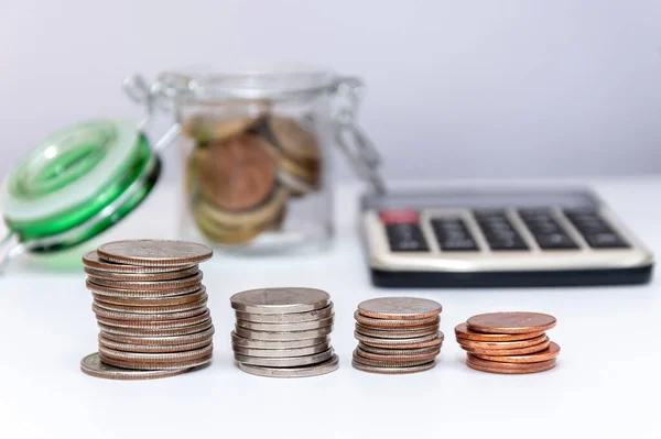 In a glass jar, metal coins, scattered change, a calculator for counting money on a white background, close-up, selective focus.Concept: financial savings, expenses and income.