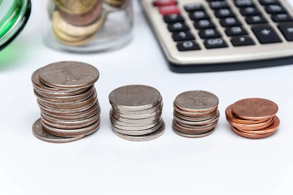 Metal coins in stacks, a calculator for counting money, a jar with small coins on a white background, close-up, selective focus.Concept: financial savings, expenses and income.