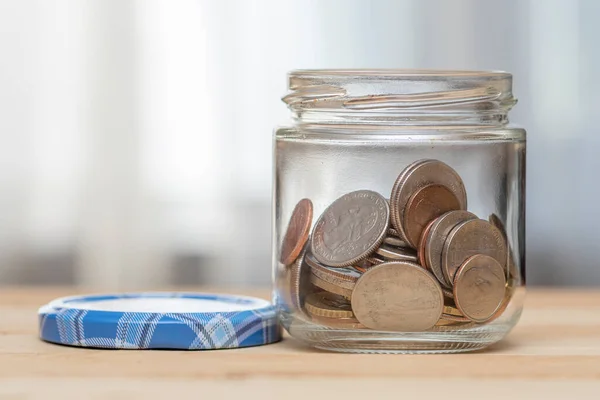 An open jar with small coins of American cents stands on a wooden table, close-up, selective focus. A concept for business and finance, savings and price increases.