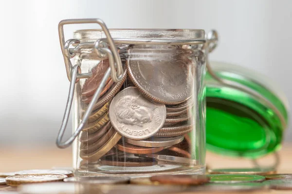 An open jar with small coins stands on a wooden table on a neutral background, close-up, selective focus. A concept for business and finance, savings and price increases.